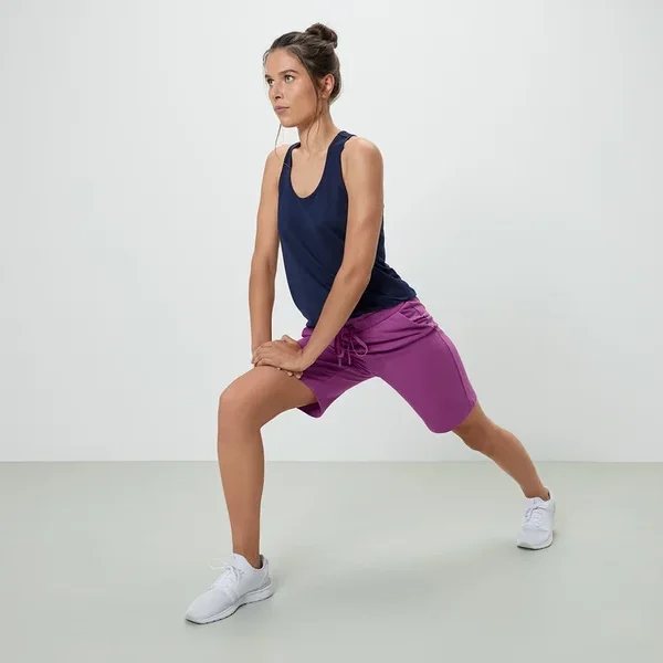 Frau dehnt sich in Tanktop und violetten Sweatshorts.