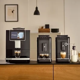 Drei »Esperto2 Caffè« Kaffeevollautomaten in verschiedenen Farben stehen nebeneinander auf einer Küchentheke. Zwei Tassen sind mit Kaffee und eine Tasse mit Milch gefüllt. Im Hintergrund befindet sich eine Milchkaraffe.