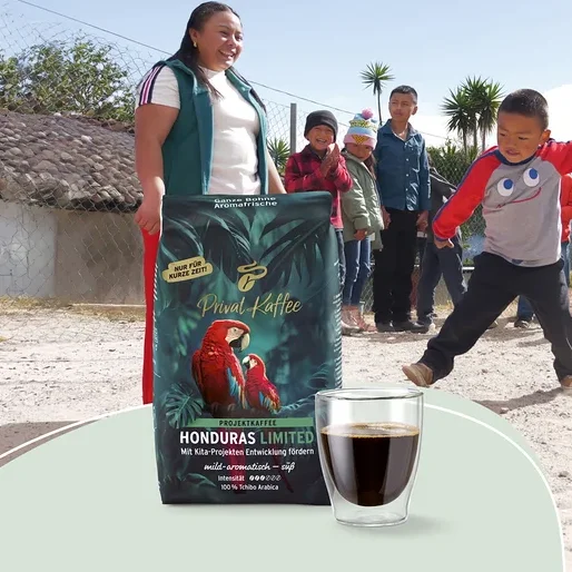 Frau und Kinder im Freien. Ein dunkelgrüner Beutel „Tchibo Privat Kaffee Honduras Limited“ mit Papageien und eine Kaffeetasse sind im Vordergrund. Ein Junge springt, andere Kinder stehen dahinter.