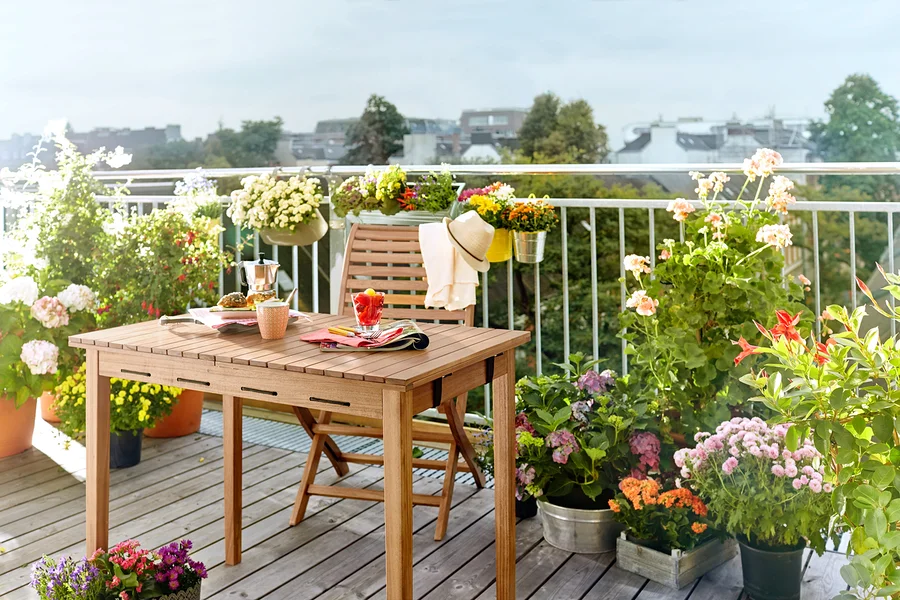 Holztisch und Stuhl auf einem Balkon, umgeben von Blumen in Töpfen.