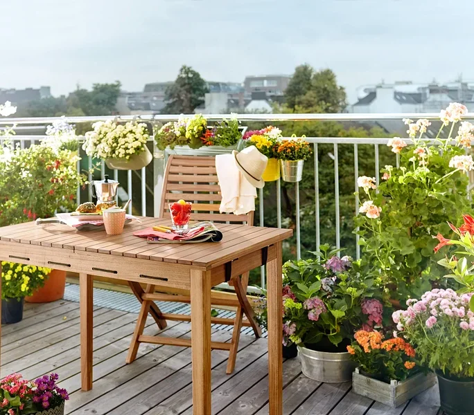 Holztisch und Stuhl auf einem Balkon, umgeben von Blumen in Töpfen.