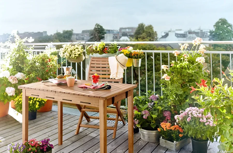 Holztisch und Stuhl auf einem Balkon, umgeben von Blumen in Töpfen.