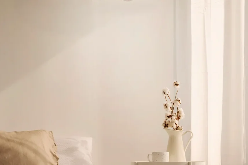 Eine strohfarbene Lampen-Hängelampe in Hutform hängt über einem Bett in einem Schlafzimmer.