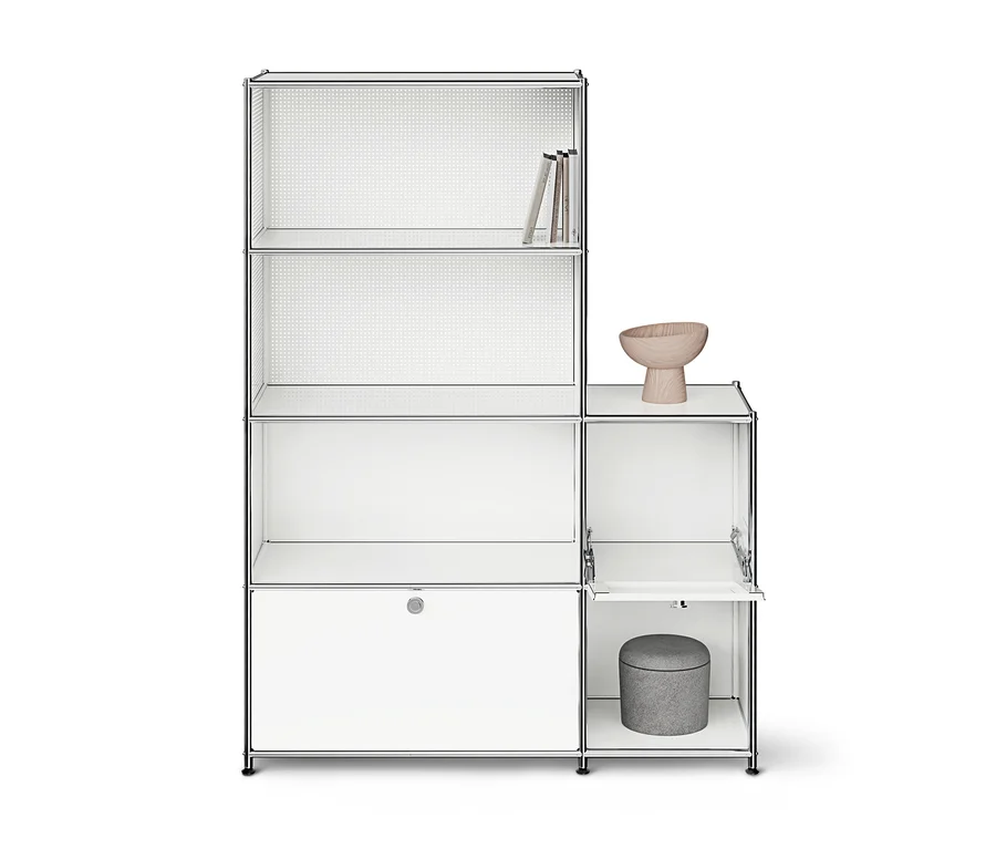 Weißes modulares Regal mit Chromrahmen und mehreren Fächern. Links drei offene Regalebenen mit Büchern oben und ein geschlossener Schrank unten. Rechts ein offenes Fach mit einer Holzschale und ein Fach mit geöffneter Klapptür, in dem ein grauer Hocker steht.