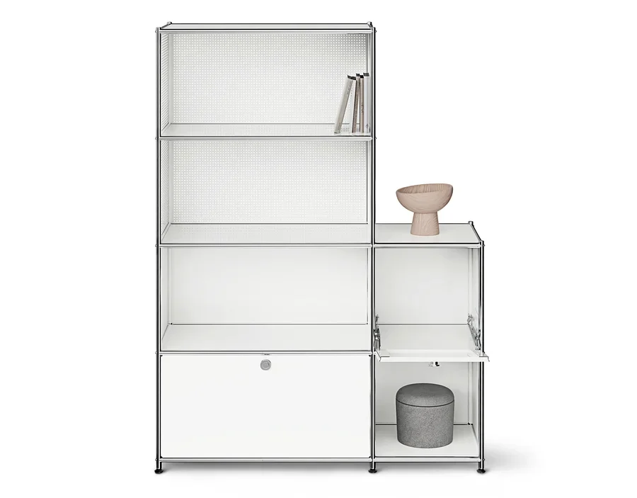 Weißes modulares Regal mit Chromrahmen und mehreren Fächern. Links drei offene Regalebenen mit Büchern oben und ein geschlossener Schrank unten. Rechts ein offenes Fach mit einer Holzschale und ein Fach mit geöffneter Klapptür, in dem ein grauer Hocker steht.