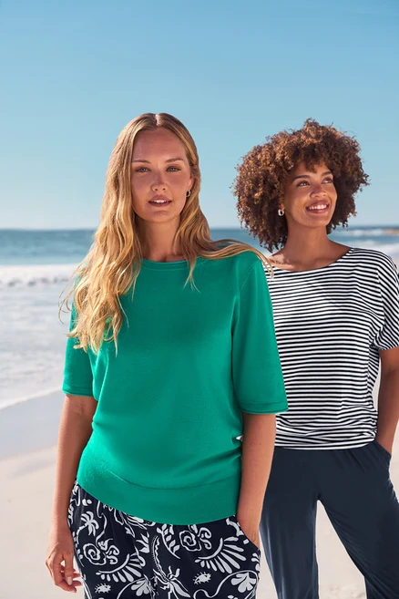 Zwei Frauen am Strand tragen Ohrstecker mit Glaskristallsteinen, Creolen Pavé und Da. 3/4-Jerseyhose, dunkelblau.