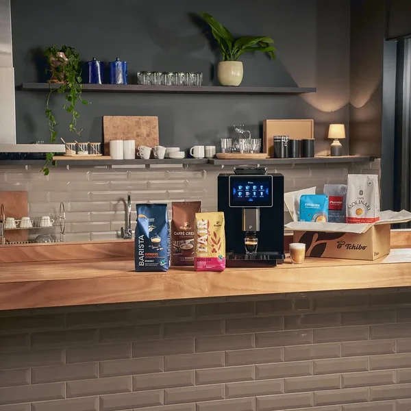 Auf einer Holzplatte stehen eine Kaffeemaschine, drei Kaffeepackungen und eine Kiste mit Kaffee.