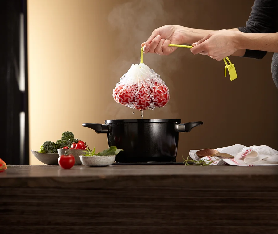Hände halten einen Beutel mit roten Beeren über einen Topf.
