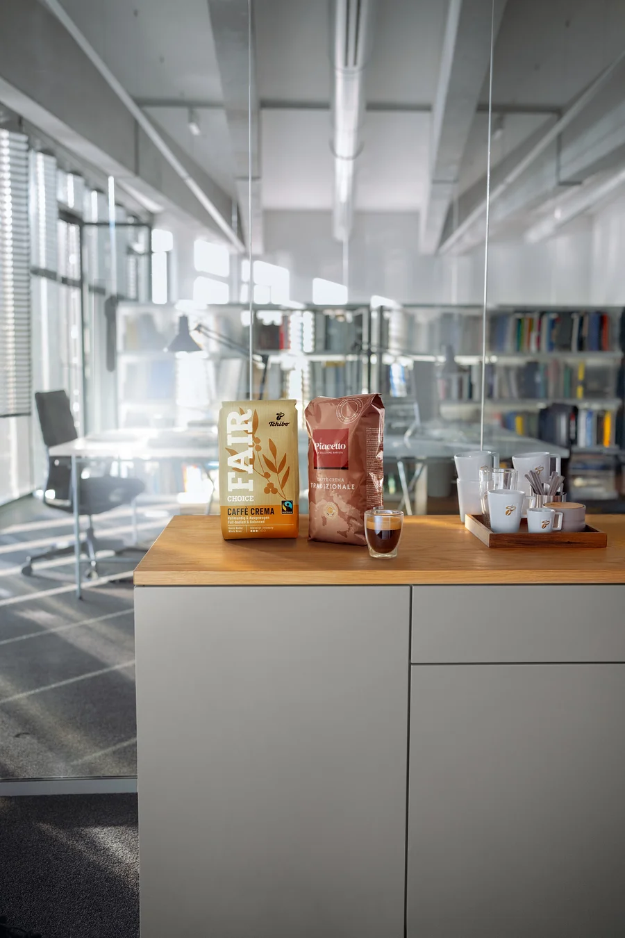 Zwei Kaffeepackungen und eine Tasse Espresso auf einer Holzplatte in einem modernen Büro.