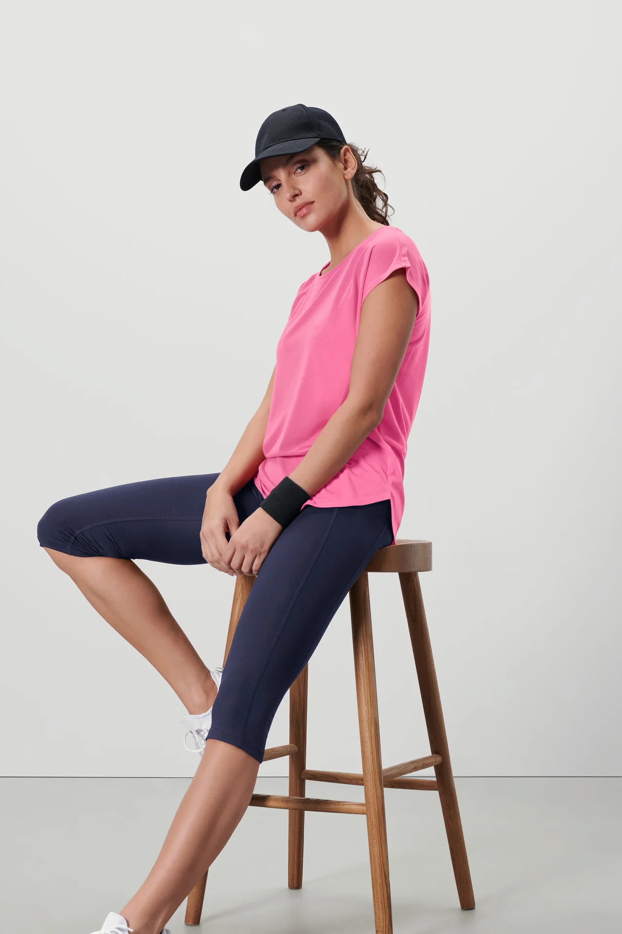 Frau sitzt auf einem Hocker und trägt ein pinkes Sportshirt.