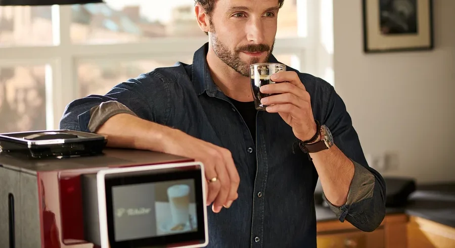 Mann trinkt Kaffee, lehnt an rotem »Tchibo Office« Kaffeevollautomat.