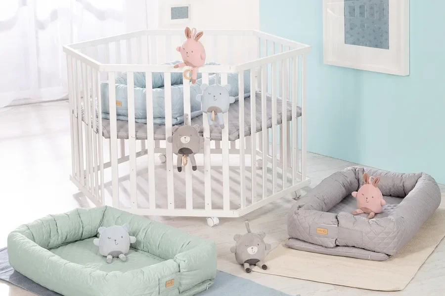 Weißes Kinderbett mit Spielzeug und zwei grüne und graue Babyschalen. Roba 3-in1-Babylounge, grün.