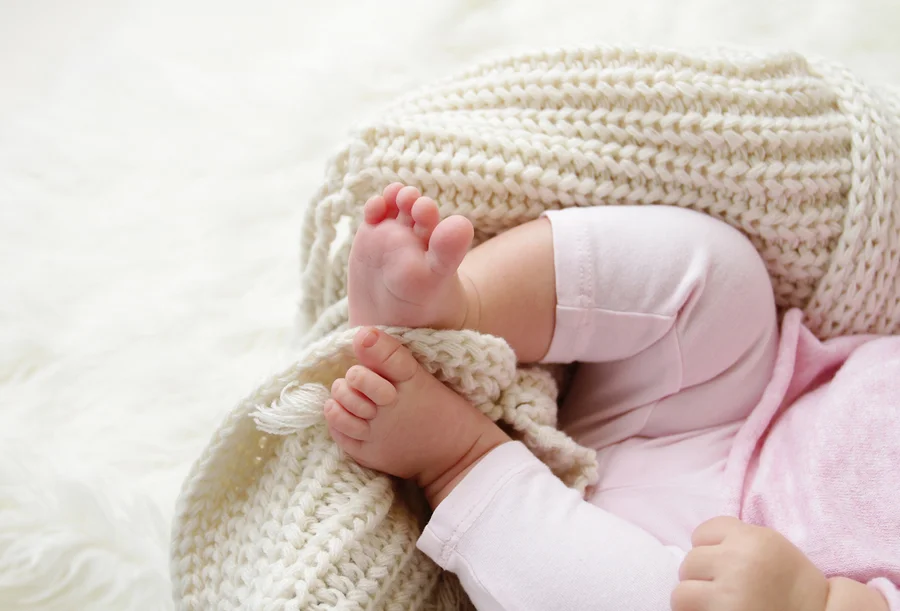 Die Füße eines Babys liegen auf einer cremefarbenen Strickdecke.