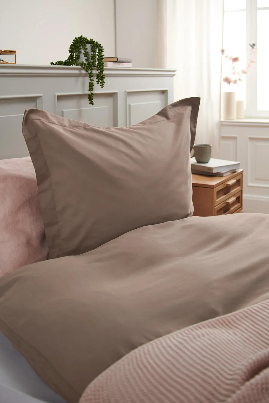 Detailaufnahme von brauner Tencel™-Baumwoll-Bettwäsche auf einem Bett mit rosa Laken.