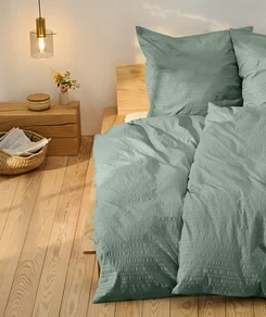 Grüne Seersucker-Bettwäsche in Normalgröße und eine in Übergröße auf einem Bett.