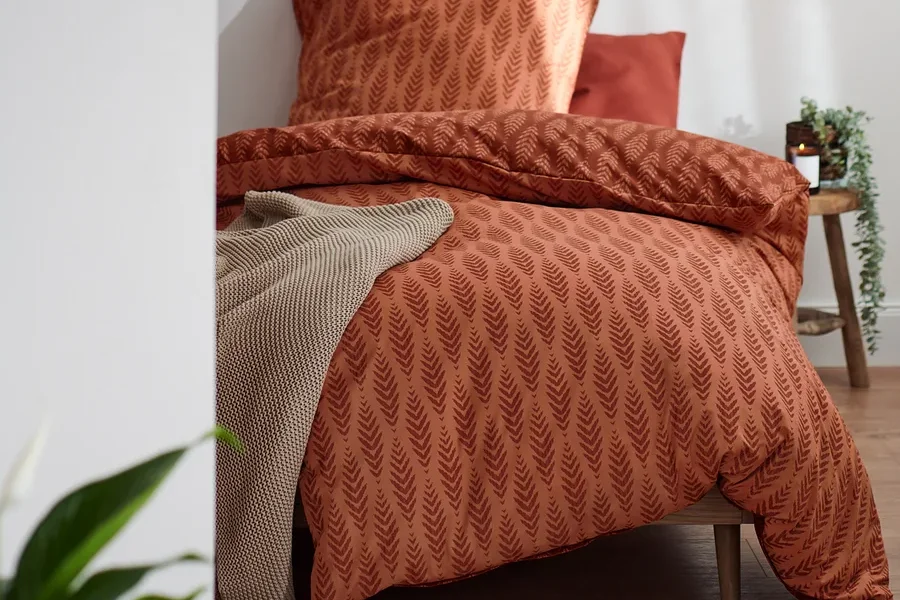 Terrakottafarbene Premium-Baumwoll-Bettwäsche in Normalgröße mit Blattmuster auf einem Bett.