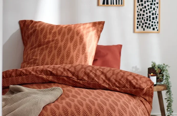 Terrakottafarbene Premium-Baumwoll-Bettwäsche in Normalgröße mit Blattmuster auf einem Bett.