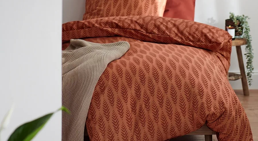 Terrakottafarbene Premium-Baumwoll-Bettwäsche in Normalgröße mit Blattmuster auf einem Bett.