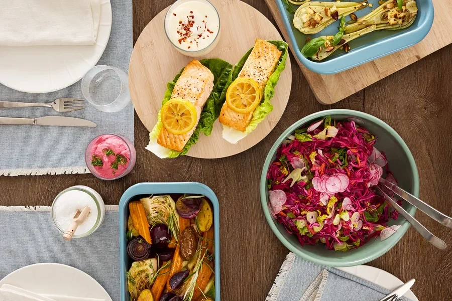 Draufsicht auf einen Holztisch mit verschiedenen Speisen, darunter Lachs, Gemüse und Salat.