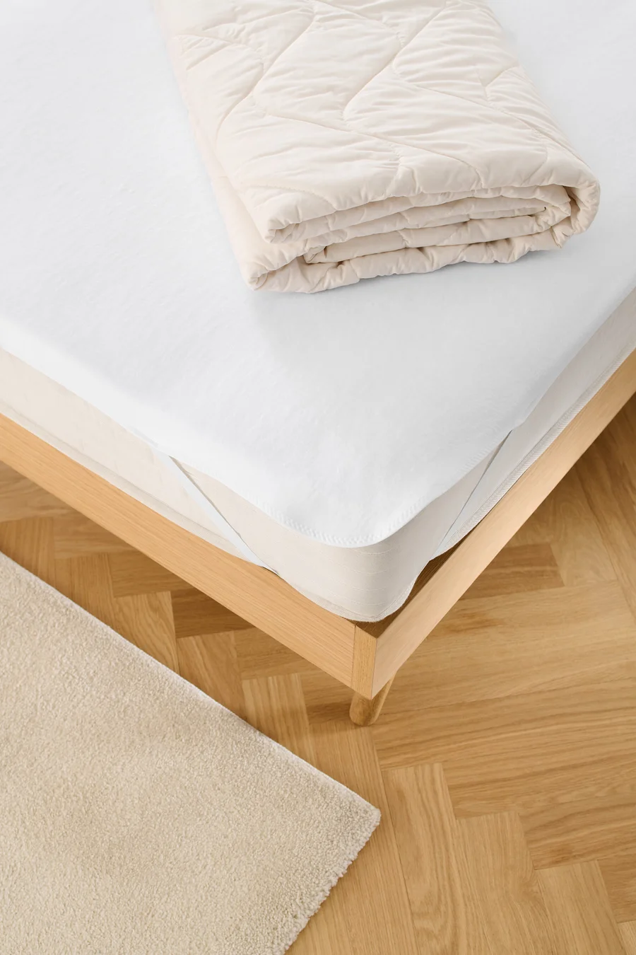 Auf einem Bett liegen ein weißer Matratzenschoner und eine gefaltete Decke.