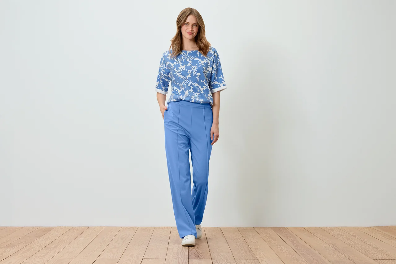 Frau posiert in hellblauem, bedrucktem Sweatshirt und blauer Hose.