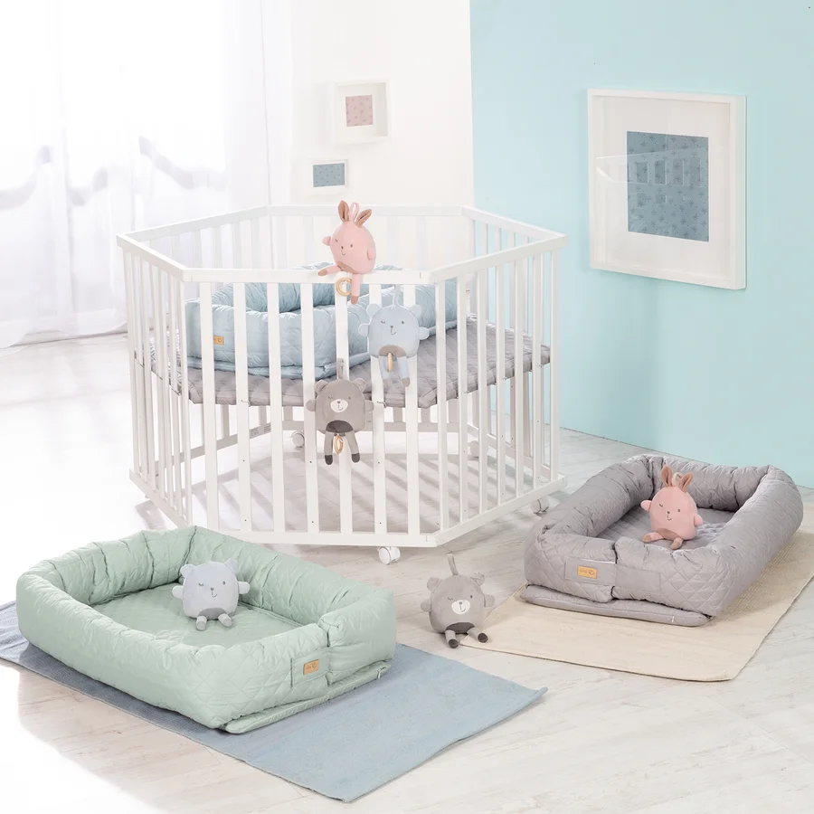 Weißes Kinderbett mit Spielzeug und zwei grüne und graue Babyschalen. Roba 3-in1-Babylounge, grün.