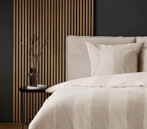 Schlafzimmer mit Bettwäsche mit beigen Streifen und grauem Teppich mit Kreismuster.