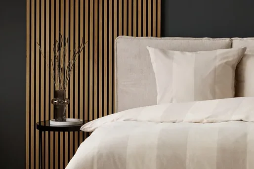 Schlafzimmer mit Bettwäsche mit beigen Streifen und grauem Teppich mit Kreismuster.