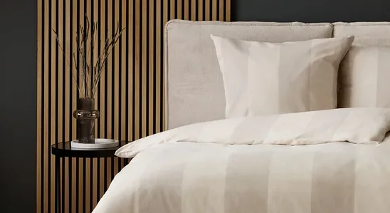 Schlafzimmer mit Bettwäsche mit beigen Streifen und grauem Teppich mit Kreismuster.