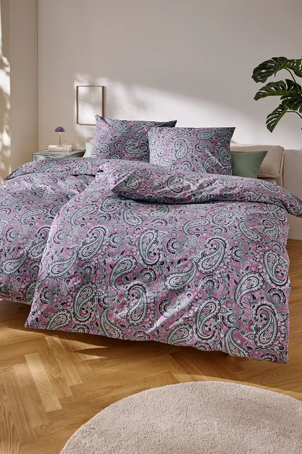 Nahaufnahme eines Bettes mit rosa Paisley-Muster-Bettwäsche.