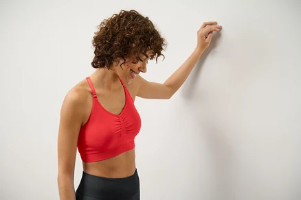 Frau lehnt an Wand und trägt rotes Seamless-Sport-Bustier.