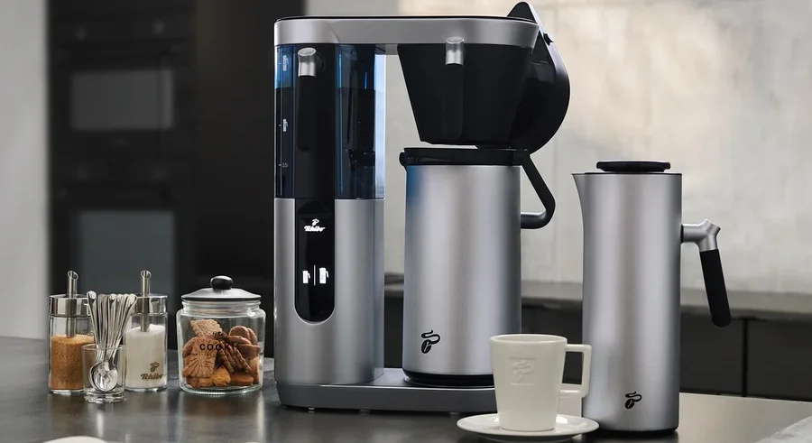 Silberne Profi-Filterkaffeemaschine Coffea Filbii neben Filbii 1L und 2L Thermoskannen. Auf dem Tisch liegen ein offenes Notizbuch und Gläser mit Zucker und Keksen.
