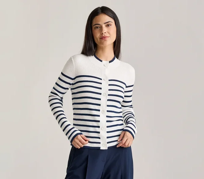 Frau mit dunkelbraunen Haaren trägt eine weiß-blau gestreifte Strickjacke mit Knöpfen und eine marineblaue Hose.