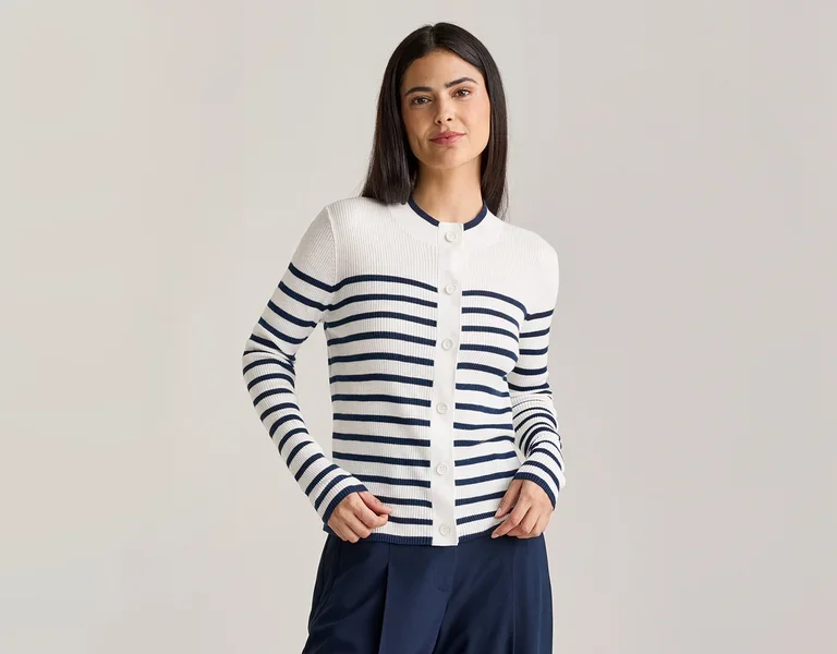 Frau mit dunkelbraunen Haaren trägt eine weiß-blau gestreifte Strickjacke mit Knöpfen und eine marineblaue Hose.
