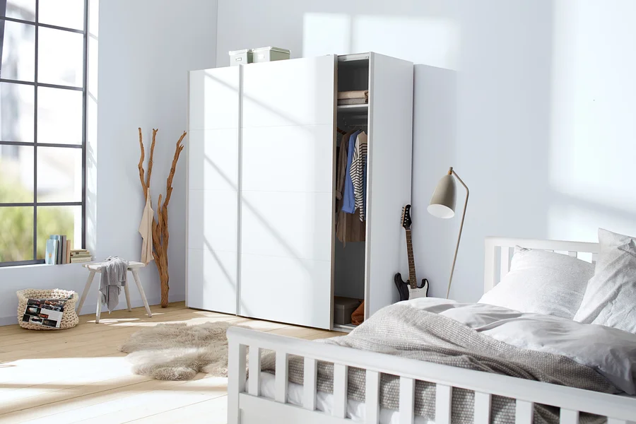 Schlafzimmer mit weißen Möbeln, darunter ein Bett und ein Schrank, mit einer Gitarre, die an den Schrank gelehnt ist.