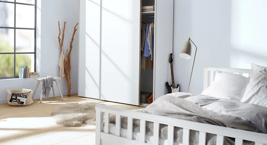 Schlafzimmer mit weißen Möbeln, darunter ein Bett und ein Schrank, mit einer Gitarre, die an den Schrank gelehnt ist.