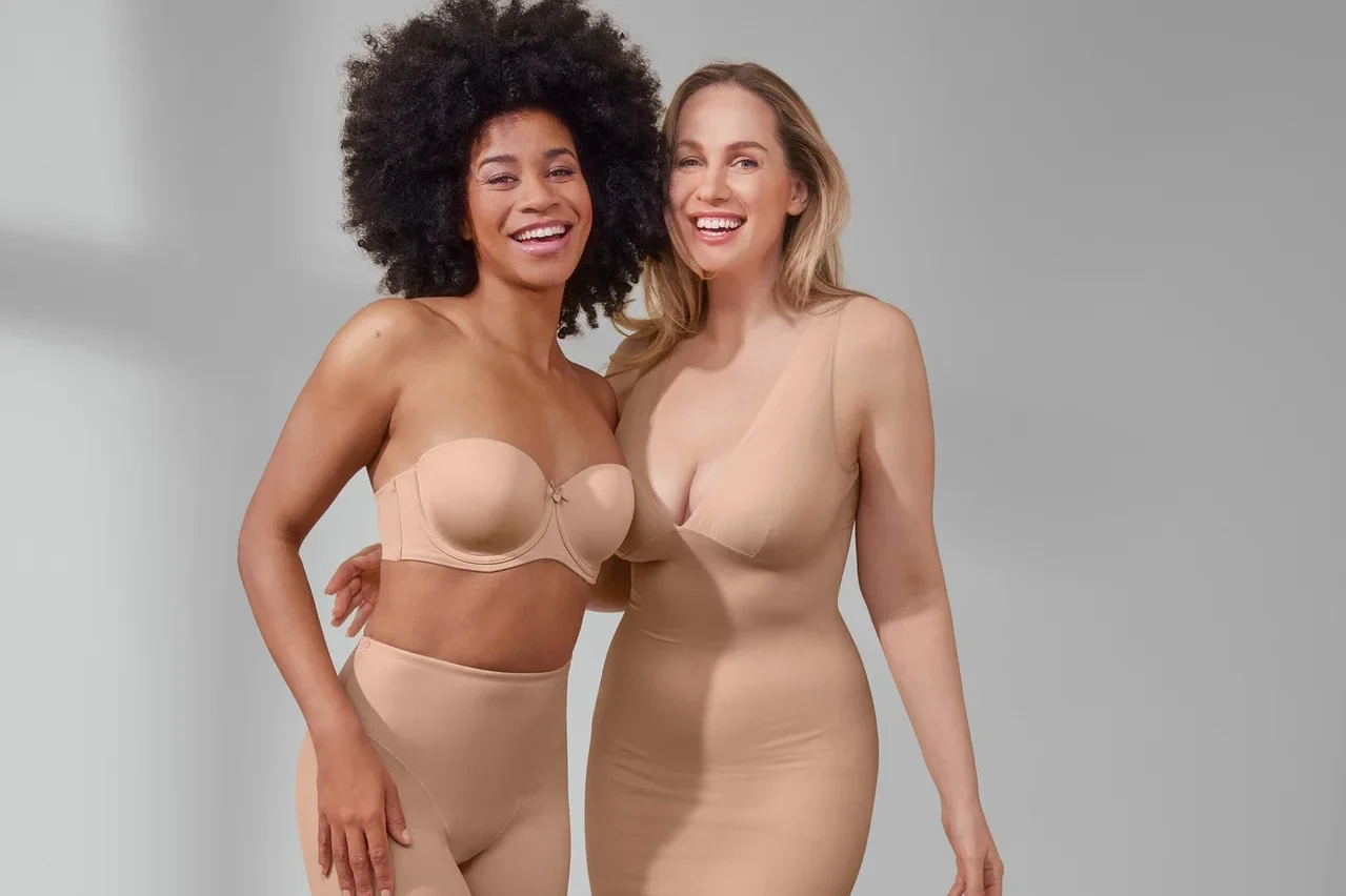 Zwei lächelnde Frauen posieren. Eine trägt einen Multistyle-BH und beige Shorts »Shaping«. Die andere trägt ein beiges Unterkleid »Shaping«.
