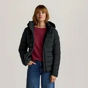 Frau steht in schwarzer Kapuzen-Steppjacke, rotem Langarmshirt, blauer weiter Jeans und schwarzen Slippern, eine Hand in der Tasche.