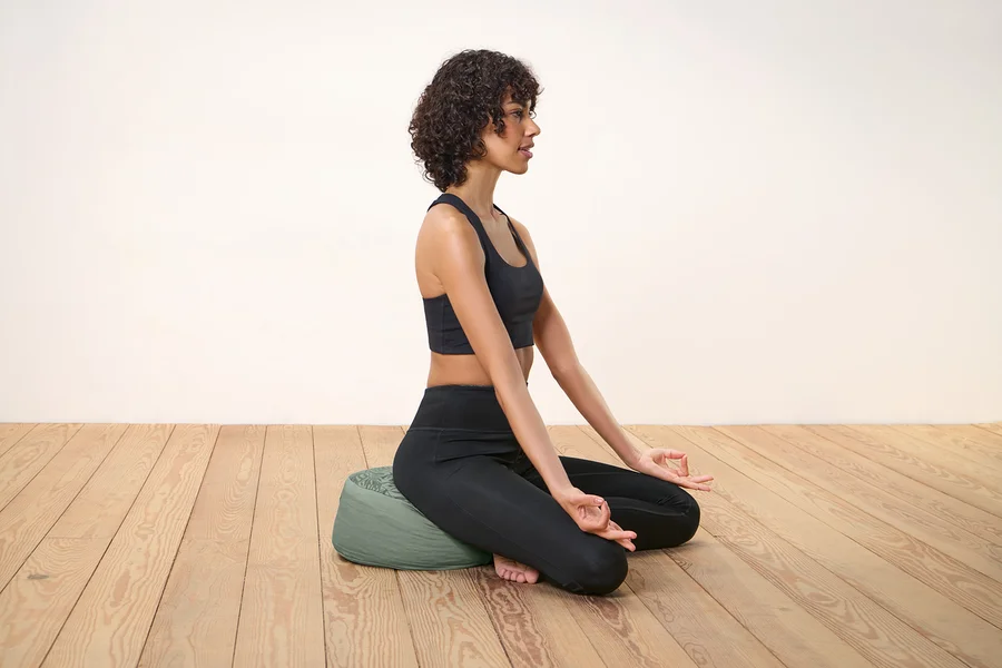 Frau sitzt auf einem Meditationskissen und macht eine Mudra.