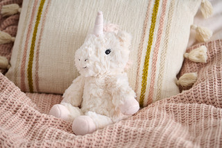 Plüschtier »Einhorn« sitzt auf einer rosa Strickdecke neben einem beigen Kissen.