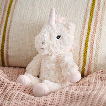 Plüschtier »Einhorn« sitzt auf einer rosa Strickdecke neben einem beigen Kissen.