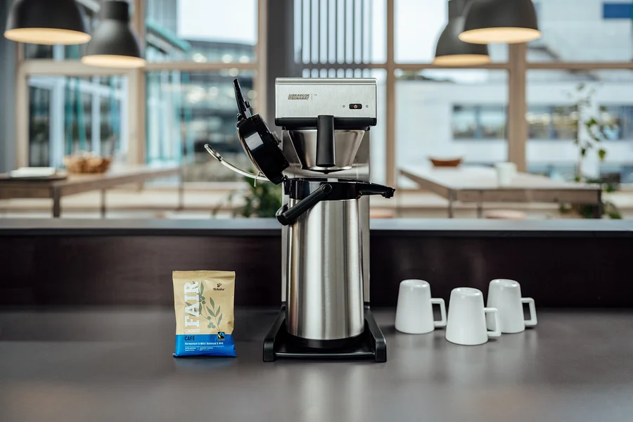 Auf einem Tisch stehen eine Profi-Filterkaffeemaschine »Bravilor-Bonamat TH« ohne Kanne, drei Tassen und eine Packung Kaffee.