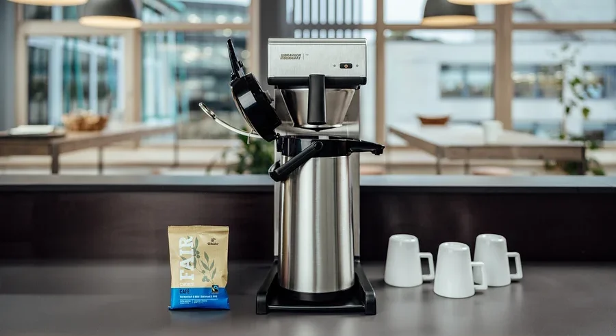 Auf einem Tisch stehen eine Profi-Filterkaffeemaschine »Bravilor-Bonamat TH« ohne Kanne, drei Tassen und eine Packung Kaffee.