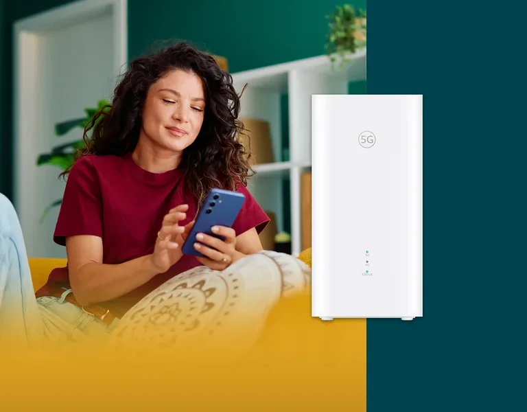 Frau mit lockigem Haar sitzt auf einem Sofa und benutzt ein blaues Smartphone. Daneben steht ein weißer 5G-Router.