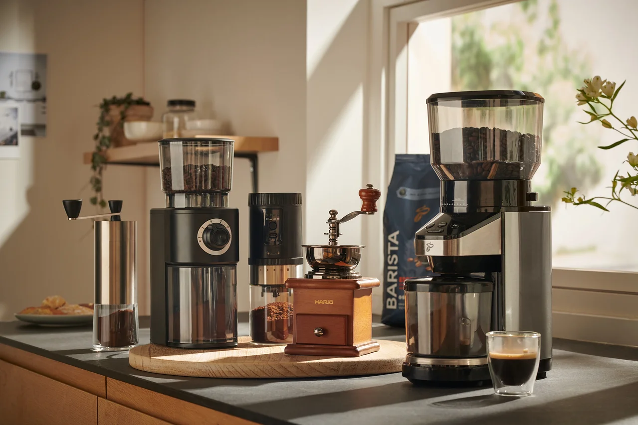 Verschiedene Kaffeemühlen, darunter Hand- und elektrische Mühlen, auf einer Küchentheke angeordnet.