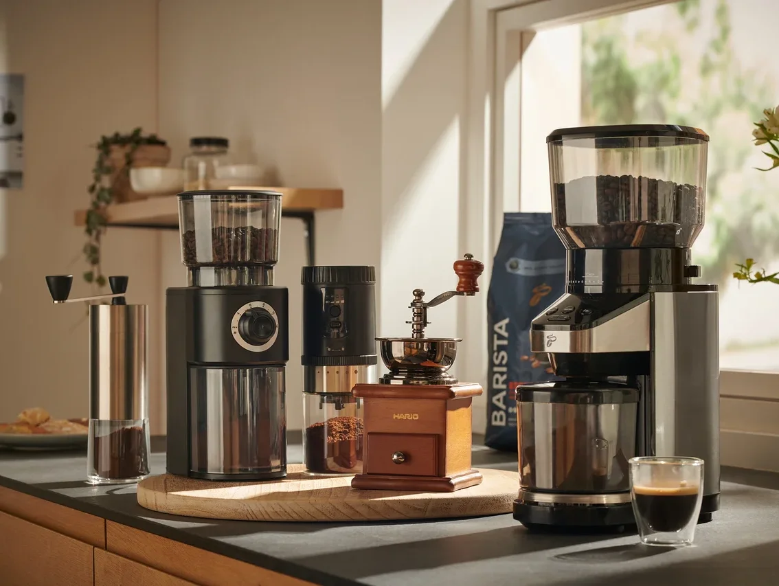 Verschiedene Kaffeemühlen, darunter Hand- und elektrische Mühlen, auf einer Küchentheke angeordnet.