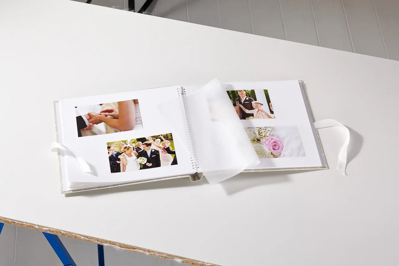 Geöffnetes Hochzeitsalbum mit Fotos auf einem weißen Tisch.