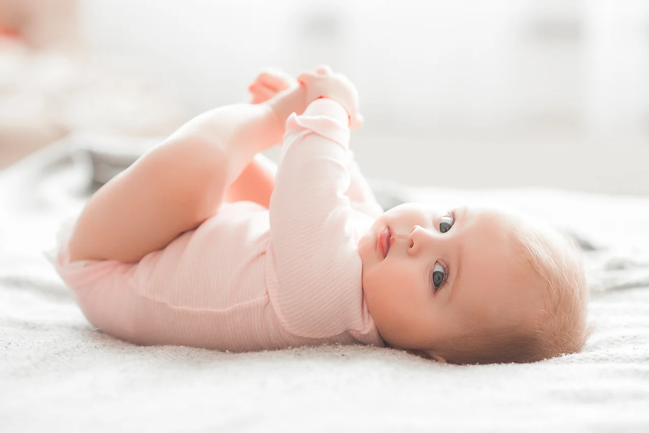 Ein liegendes Baby in rosa Kleidung hält seine Füße.