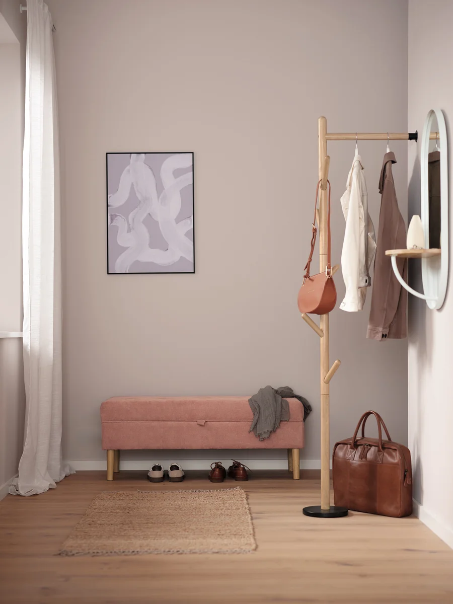 Flur mit rosa Bank, Schuhen, braunem Teppich, Garderobenständer, Handtasche und Spiegel.