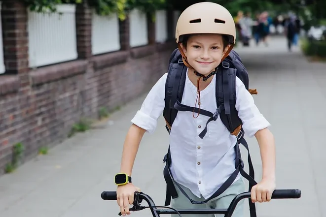 Junge mit Rucksack und beigem Helm fährt mit dem Fahrrad auf dem Gehweg.